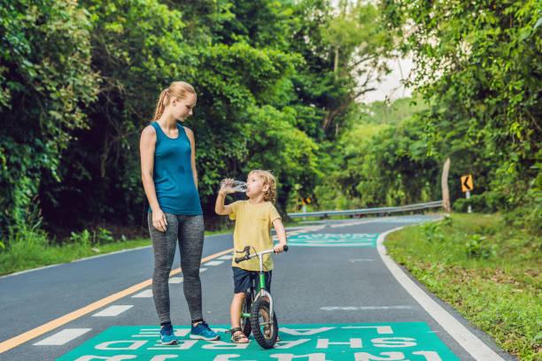 日の出時に道路を走るスポーティな女性。息子は自転車のバランスを取りに行く。フィットネスとワークアウトのウェルネスコンセプト - 2603 ストックフォトと画像