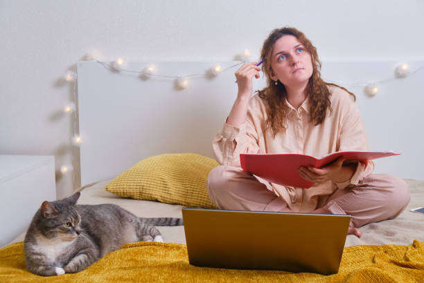 Problems with online education from home. Sad woman sitting with laptop on bed with cat