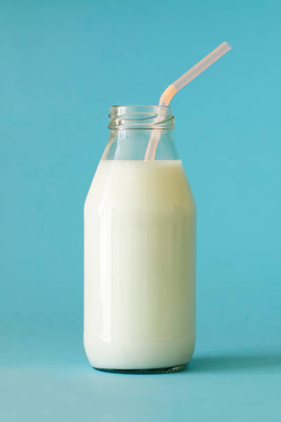 Fresh farm milk in glass bottle with pink color tubule on blue background close up front view. Milk in glass bottle to the top. Milk is good for children's health and saturates body with calcium and vitamin D leche de granja fresca en botella de vidrio con tubulo de color rosa sobre fondo azul cerca de la vista frontal. leche en botella de vidrio hasta la parte superior. la leche es buena para la salud de los niños y satura el cuerpo con calcio y vitamina d