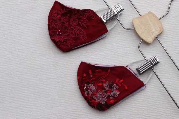 Photo of Ruby Red color of lace reusable face masks hanging on clothes hanger placed on brown background.