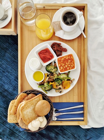 A breakfast plate with grilled vegetables, bread, toast and typical mediterranean bites such as goat's cheese, tomaoe conserve and olive oil served on a tray in bed