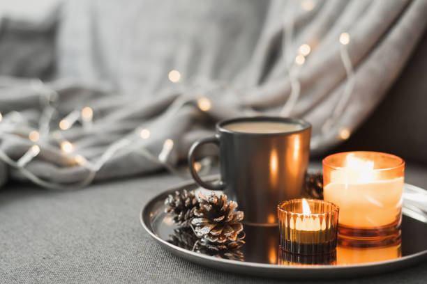 istock Two burning aroma candles, coffee in a black mug and decorative pine cones served on a round metal tray. Cozy atmosphere. Hygge concept 1257572864