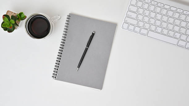 istock Workspace at home with white table. Top view from above of notebook with keyboard, earphone and coffee. 1257573984