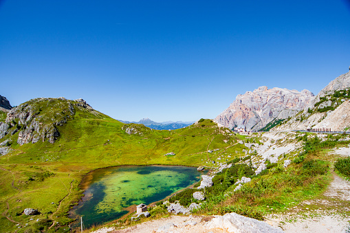 Italian mountains and green lake near the Langkofel Group, and green meadows on a sunny cloudless day.