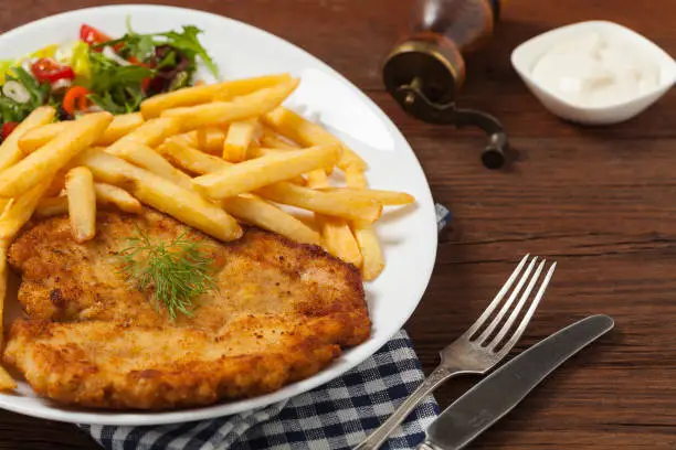 Chicken schnitzel, served with fries and salad. Natural wooden background. Front view.