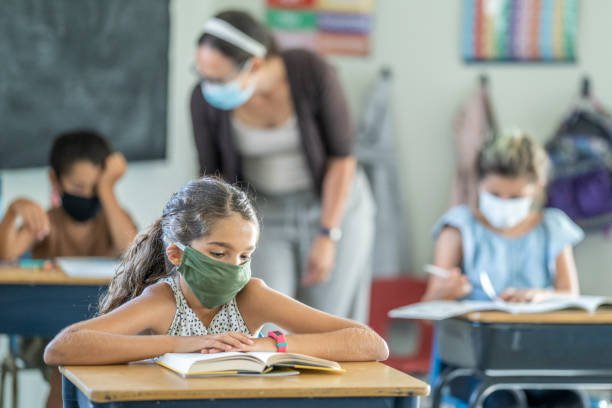 Young female student wearing a protective face mask in the classroom 12 year old girl wearing a reusable, protective face mask in classroom while working on school work at her desk. mediterranean ethnicity stock pictures, royalty-free photos & images