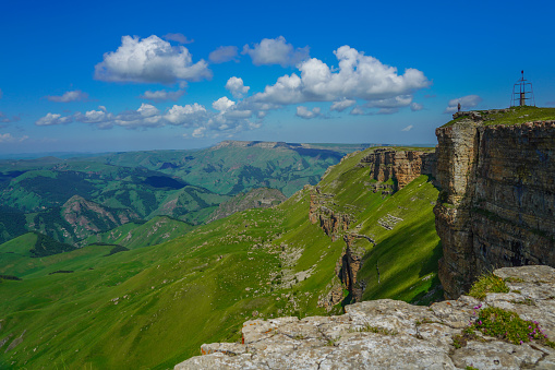 Man Stands on the Abyss at the Amazing Bermamyt Plateau. Caucasus Elbrus Region in Russia Summer Landscape with green Meadow, Panorama dramatic Sky