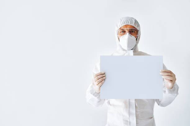 istock Doctor in protective medical suit showing blank placard with copy space for text 1257583482
