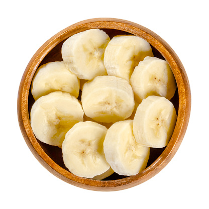 Fresh banana slices in wooden bowl. Ripe and peeled banana cut into round pieces. Edible and ready to eat dessert fruit with slightly yellow color. Closeup from above, over white, isolated food photo.