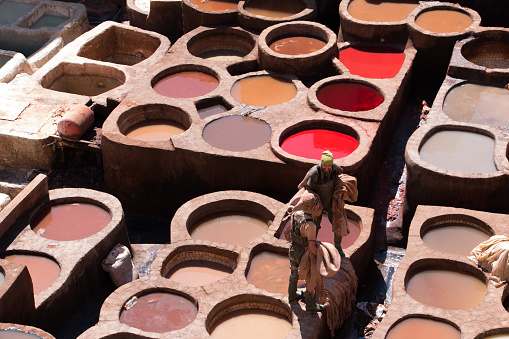 Fez, Morocco - March 9, 2018: Men working between stone vessels with dyes and leathers in a traditional tannery in the city of Fez, Morocco. Traditional workers