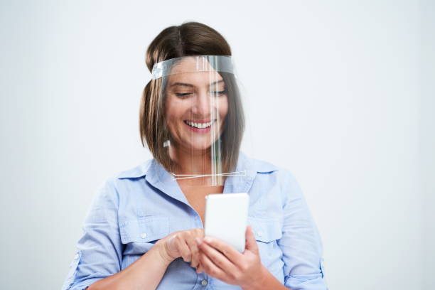 istock Woman wearing protective mask holding smartphone over white background 1257587399