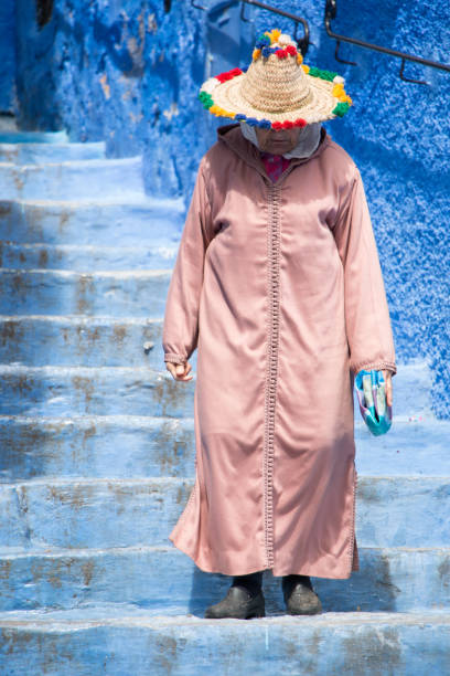 An old woman strolls through the streets of Chefchaouen, the blue town in Morocco, with her traditional costume stock photo
