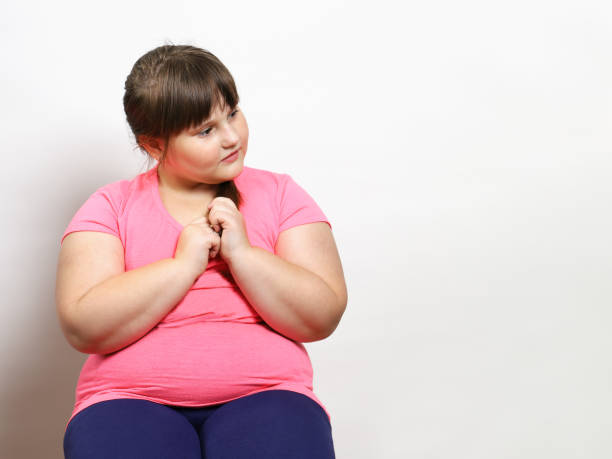 Little plump girl sits and looks to the side in thought Little plump girl sits and looks to the side in thought. Problem of excess weight in children, after quarantine. On light background with copy space overweight child stock pictures, royalty-free photos & images