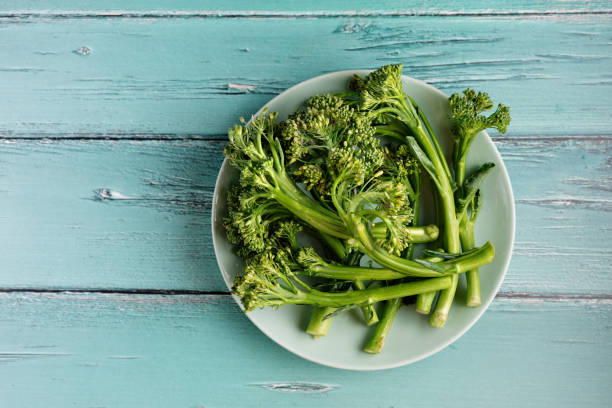 istock Top view of a green plate with broccolini on rustic light blue background 1257590543
