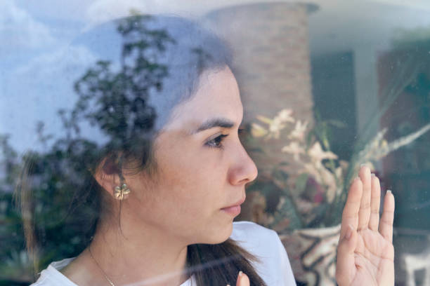 istock Lockdown Hispanic young woman looking through window 1257591737