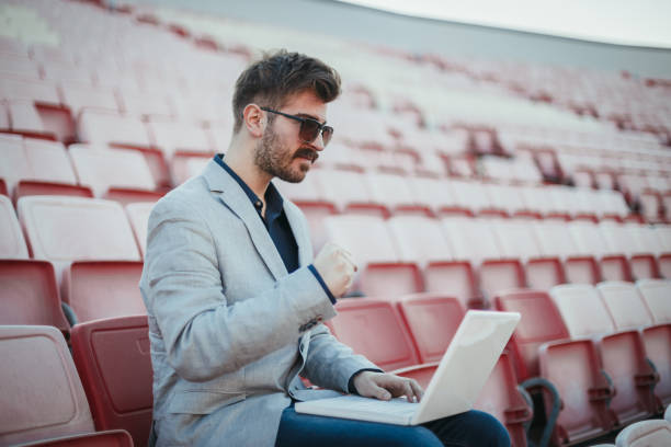 istock Young man using laptop on an empty football stadium 1257600418