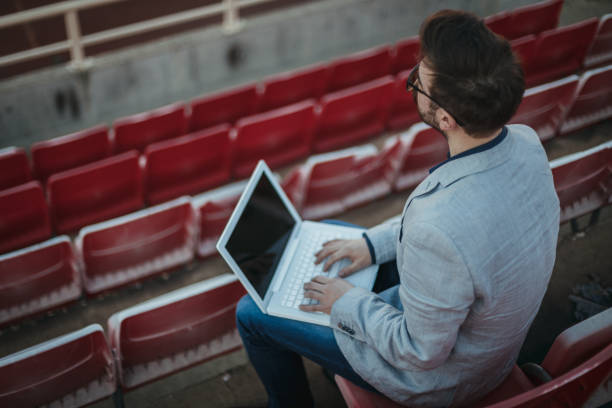 istock Young man using laptop on an empty football stadium 1257600460