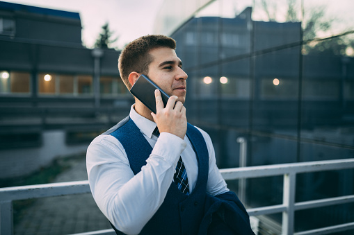 Young businessman standing in front of the office building and using smartphone outdoors