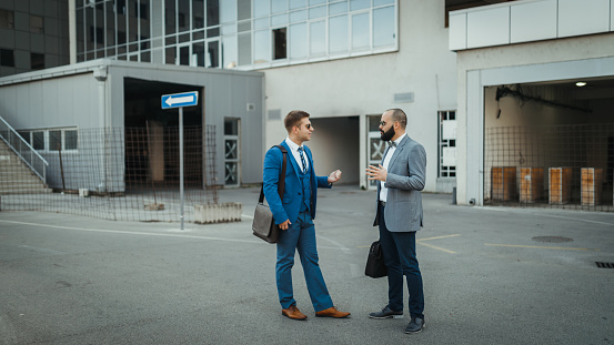 Two fashionable young millennial businessmen talking in front of the office building outdoors