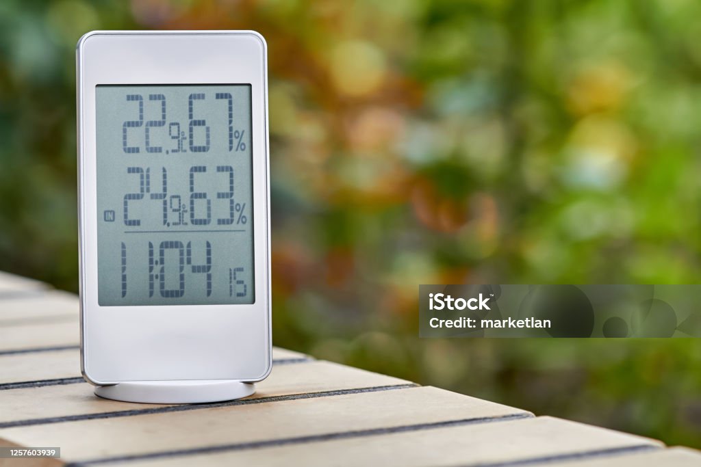 Best personal weather station device with weather conditions inside and outside on foliage background. Home digital weather forecast concept with temperature and humidity. Digital Clock Stock Photo