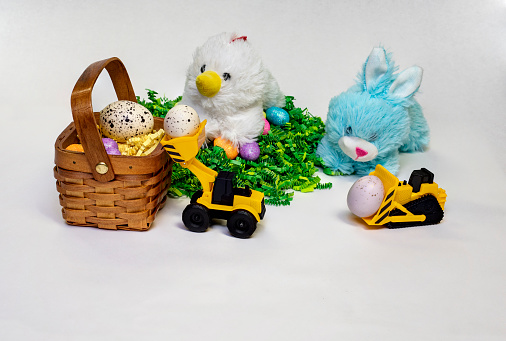 Easter themed photo of stufed bunny and hen with decorated Easter eggs, a basket,  and a child's toy construction vehicles.