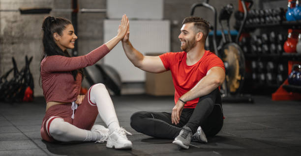 Happy female athlete having fun while giving her boyfriend high-five on a break in a gym Happy female athlete having fun while giving her boyfriend high-five on a break in a gym images of female bodybuilders stock pictures, royalty-free photos & images