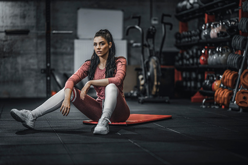 Portrait of serious sporty woman sitting on exercise mat in the gym