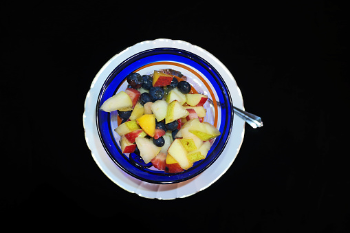 Fruit salad in a fancy cocktail glass on a white plate - view from above.