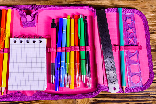 Different school stationeries (pens, pencils, notepad, ruler and protractor) in pink pencil box. Top view