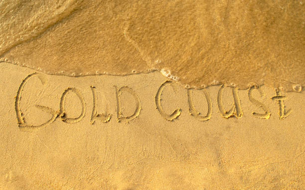 Gold Coast words written on beach sand with water wave stock photo