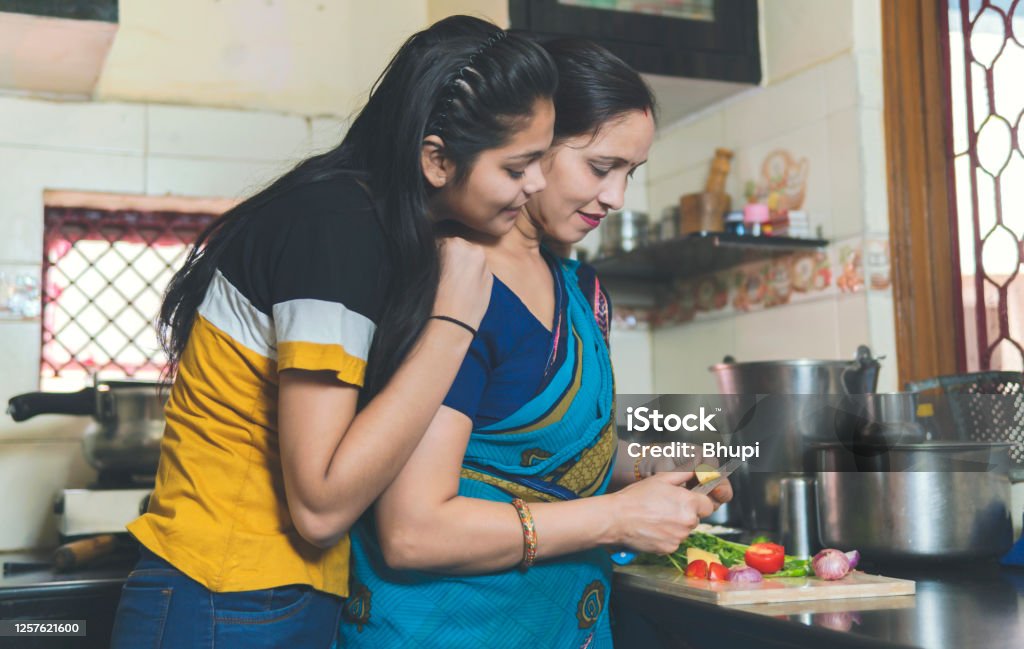 Indian mother is teaching her daughter how to chop vegetable and Daughter helping mother in kitchen. India Stock Photo