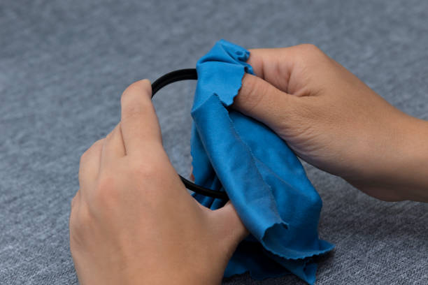 istock Women's hands wiping the protective photo filter with a blue microfiber cloth on a gray fabric background. Care for optics. Cleaning the glass. 1257621650