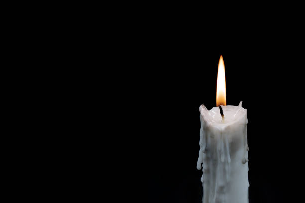 White candle on dark background. Memory photo. One candle with fire on black. In memoriam banner template with text place. White wax candle for memory of gone relatives. Memory day card backdrop White candle on dark background. Memory photo. One candle with fire on black. In memoriam banner template with text place. White wax candle for memory of gone relatives. Memory day card backdrop melting wax stock pictures, royalty-free photos & images