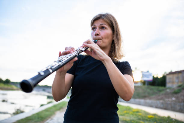 una mujer tocando el oboe en la orilla del río - oboe fotografías e imágenes de stock