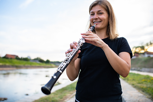 A woman is playing an oboe by the river