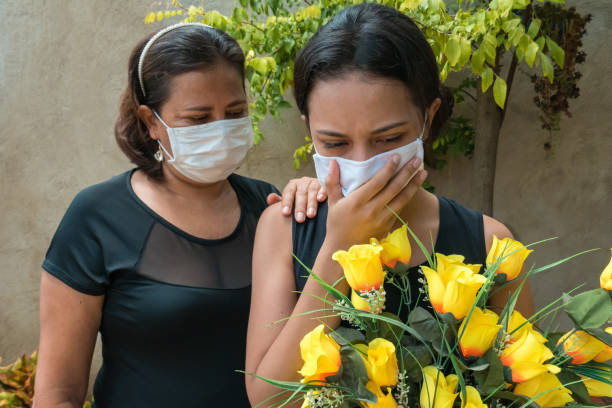 woman mourning, wearing black and holding flowers, someone puts a hand on her to console - funeral family sadness depression imagens e fotografias de stock