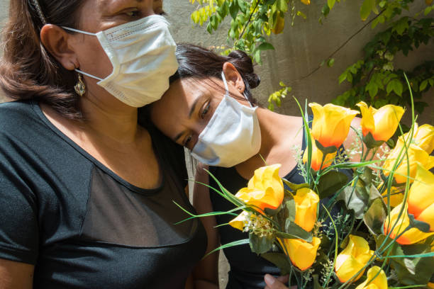 mother and daughter mourning those lost to the coronavirus, wearing face masks, showing mutual support, hugging - funeral family sadness depression imagens e fotografias de stock