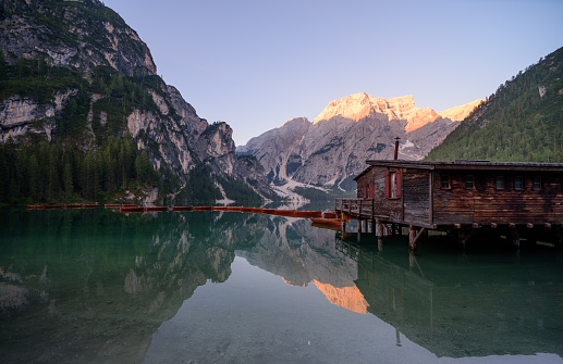 The Seekofel mountains and wooden boats reflected in the waters of Lake Braies at first light in the morning, in the Pragser Wildsee also called Lake Prags you can also see a hut, mountain landscape in the Italian Dolomites in South Tyrol