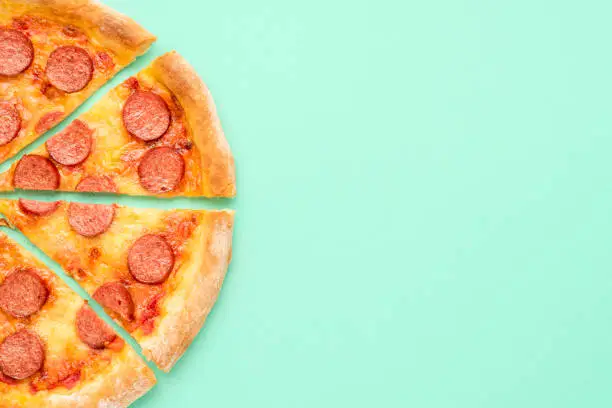 Above view with a pepperoni pizza on a green-mint background. Sliced pizza isolated on a green colored table. Home-baked pizza