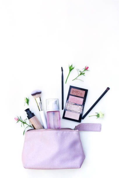 vários produtos cosméticos e flores em um saco rosa no fundo branco - cosmetic bag - fotografias e filmes do acervo