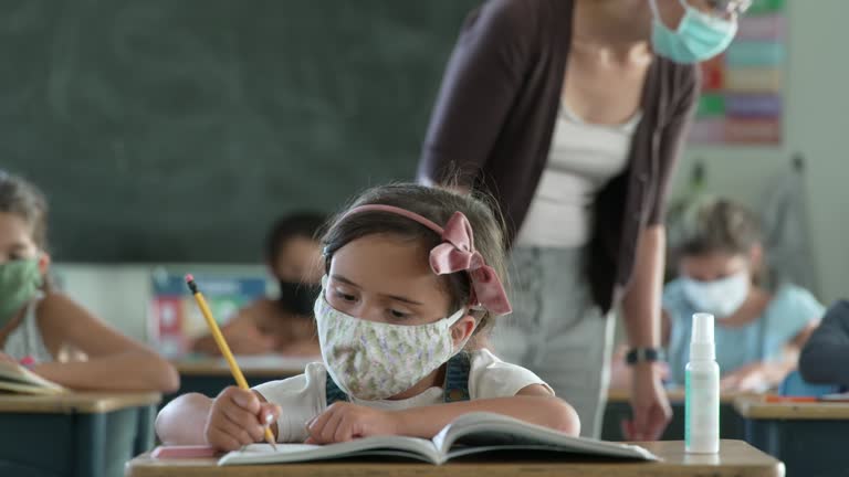 Group of students working at their desks in class all wearing protective face masks to avoid the transfer of germs after school reopened after COVID-19.