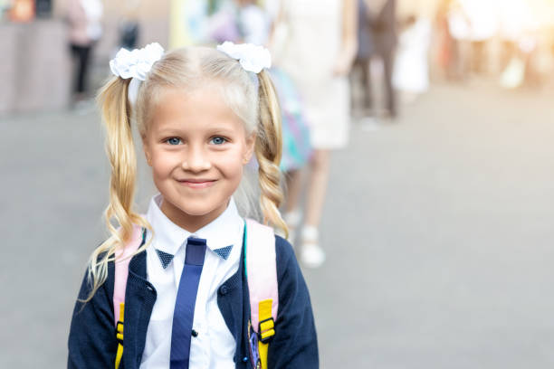 portrait of cute adorable little caucasian school girl with funny blond pig-tails hair wearing uniform and backpack enjoy going back to school. first class primary elementary education happy pupil - blond hair carrying little girls small imagens e fotografias de stock