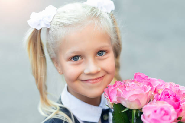 portrait of cute adorable little caucasian school girl with funny blond pig-tails hair wearing uniform and flowers bouquet going back to school. first class primary elementary education happy pupil - blond hair carrying little girls small imagens e fotografias de stock