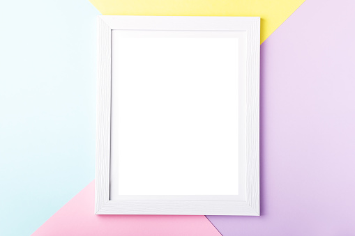 White picture frame on pastel multicolor geometric background. Mockup on colorful table top, copy space, top view