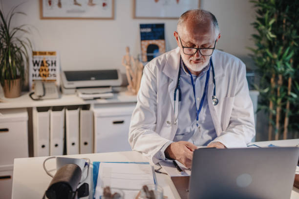 istock Mature male doctor using phone in his office at night 1257645504