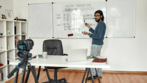 istock Javascript lesson. Young bearded male teacher wearing glasses pointing at whiteboard and teaching Javascript, giving lesson online. Recording video blog 1257646871