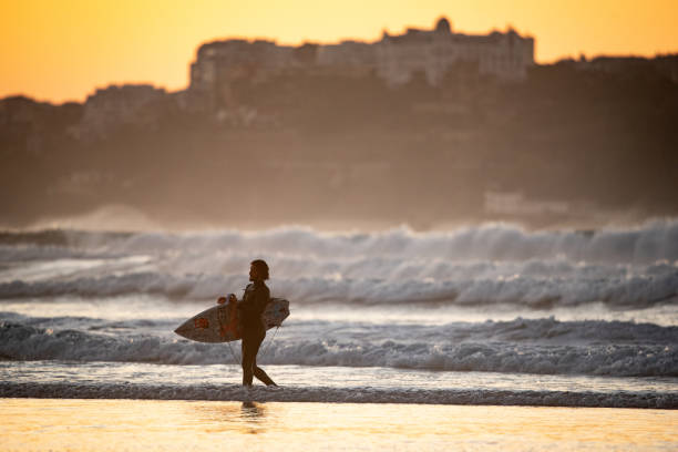 surfer holding surf board at wave beach of Somo where the city of Santander is seen in the background. Somo, Cantabria.