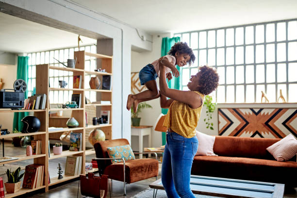 Afro-Caribbean Mother and Young Daughter Playing at Home Carefree single mother in mid 20s lifting 3 year old daughter and laughing as they enjoy relaxed time in home interior. retrieving stock pictures, royalty-free photos & images