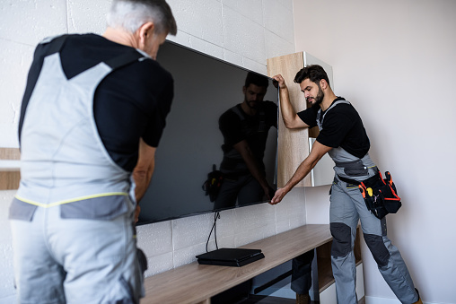 Dos técnicos profesionales, trabajadores de uniforme instalando televisión en la pared interior. Concepto de construcción, mantenimiento y entrega photo