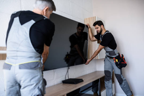 Two professional technicians, workers in uniform installing television on the wall indoors. Construction, maintenance and delivery concept